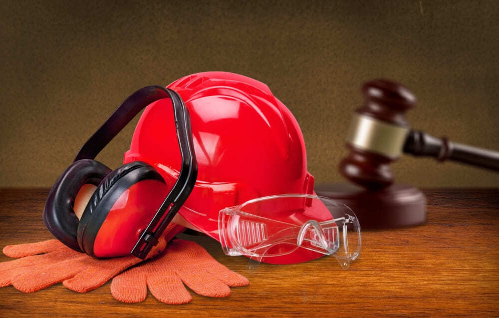 Red construction helmet, safety gloves, protective goggles, and earmuffs representing construction worker safety and legal protections in New York